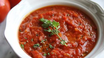 Homemade tomato sauce in a saucepan with fresh basil and garlic cloves on the side.