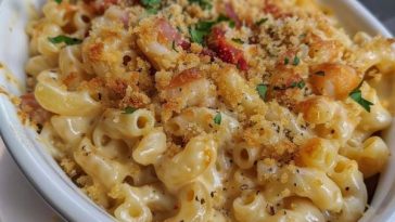A bubbling dish of crab mac and cheese with golden breadcrumbs, creamy sauce, and chunks of crab meat, garnished with herbs.