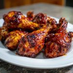 Juicy oven BBQ chicken drumsticks glazed with sticky barbecue sauce, served on a baking tray with fresh herbs and dipping sauce.