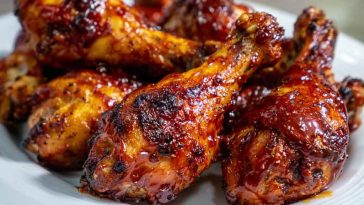 Juicy oven BBQ chicken drumsticks glazed with sticky barbecue sauce, served on a baking tray with fresh herbs and dipping sauce.