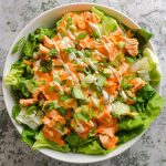A bowl of buffalo chicken salad with spicy grilled chicken, crisp romaine, celery, cherry tomatoes, and a drizzle of ranch dressing.