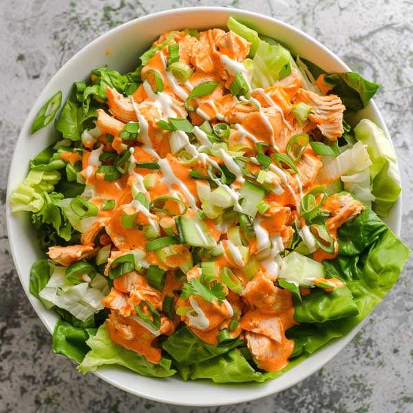 A bowl of buffalo chicken salad with spicy grilled chicken, crisp romaine, celery, cherry tomatoes, and a drizzle of ranch dressing.