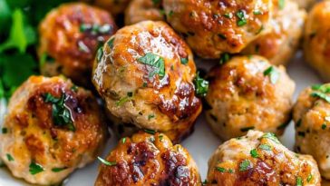 Golden-brown chicken meatballs garnished with herbs, served on a plate with dipping sauce.