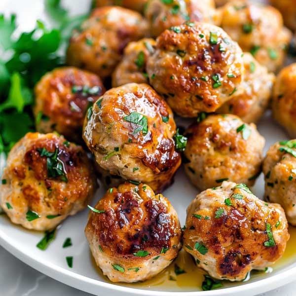 Golden-brown chicken meatballs garnished with herbs, served on a plate with dipping sauce.