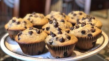 Freshly baked banana chocolate chip muffins on a cooling rack with chocolate chips scattered around.