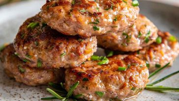 Homemade turkey sausage patties cooked to golden perfection, served on a plate with herbs and a side of eggs for breakfast.