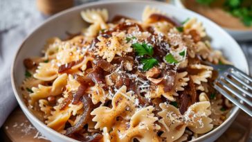 Creamy caramelised French onion pasta topped with golden onions, parmesan cheese, and fresh herbs in a serving bowl.