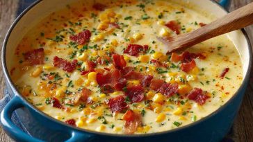 A warm bowl of creamy cheddar corn chowder topped with shredded cheese and fresh herbs, served with crusty bread.