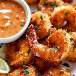 Crispy golden coconut shrimp served with a creamy dipping sauce in a small bowl, garnished with lime wedges.