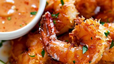 Crispy golden coconut shrimp served with a creamy dipping sauce in a small bowl, garnished with lime wedges.