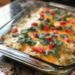 A bubbling casserole dish filled with layers of shredded chicken, green chiles, tortillas, and melted cheese, garnished with cilantro.