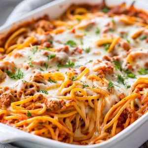 A casserole dish of baked spaghetti with layers of pasta, marinara sauce, ground beef, and melted cheese, garnished with fresh parsley.