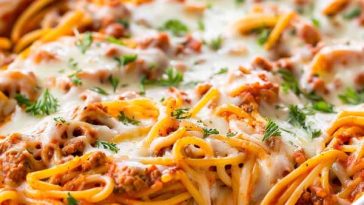 A casserole dish of baked spaghetti with layers of pasta, marinara sauce, ground beef, and melted cheese, garnished with fresh parsley.