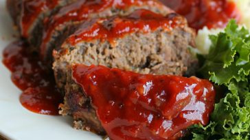 A slice of tender, juicy meatloaf topped with a rich glaze, served with mashed potatoes and green beans on a dinner plate.
