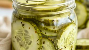 Crisp homemade sliced dill pickles in a glass jar with garlic, fresh dill, and spices in a clear brine.