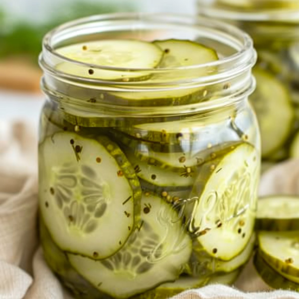 Crisp homemade sliced dill pickles in a glass jar with garlic, fresh dill, and spices in a clear brine.