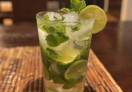 A refreshing glass of mojito cocktail with lime wedges, mint leaves, and ice cubes, served in a tall glass.