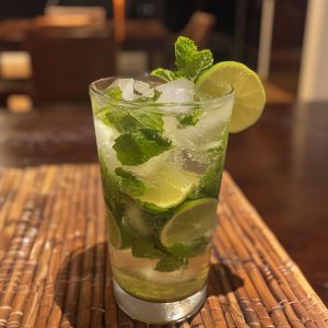 A refreshing glass of mojito cocktail with lime wedges, mint leaves, and ice cubes, served in a tall glass.