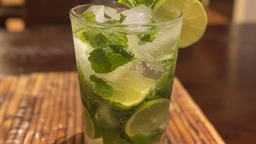 A refreshing glass of mojito cocktail with lime wedges, mint leaves, and ice cubes, served in a tall glass.
