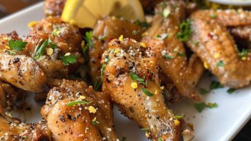 Crispy golden lemon pepper chicken wings served on a platter, garnished with fresh lemon slices and parsley.