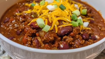 Hearty bowl of chili topped with cheese and fresh herbs.