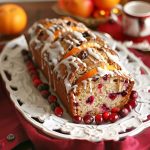 Moist cranberry bread topped with sweet orange glaze, sliced and garnished with fresh cranberries and orange zest.