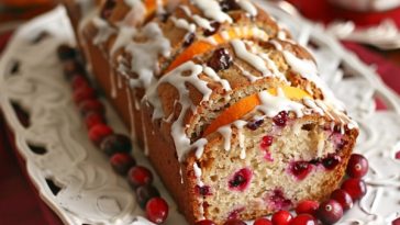 Moist cranberry bread topped with sweet orange glaze, sliced and garnished with fresh cranberries and orange zest.