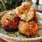 Golden crispy arancini rice balls filled with gooey cheese and rice, served with marinara sauce for dipping.