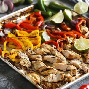 Colorful sheet pan chicken fajitas with sliced bell peppers, onions, and seasoned chicken strips fresh out of the oven.