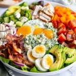 A vibrant Cobb salad bowl filled with grilled chicken, crispy bacon, hard-boiled eggs, avocado, tomatoes, blue cheese crumbles, and drizzled with creamy homemade dressing.