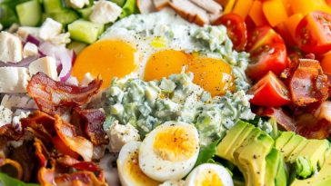 A vibrant Cobb salad bowl filled with grilled chicken, crispy bacon, hard-boiled eggs, avocado, tomatoes, blue cheese crumbles, and drizzled with creamy homemade dressing.