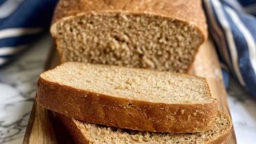 A loaf of simple whole wheat bread with a golden crust, sliced to reveal its soft, hearty crumb.