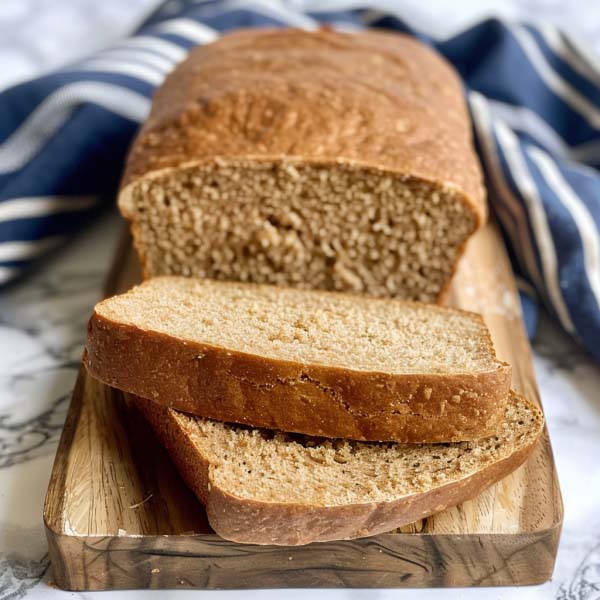 A loaf of simple whole wheat bread with a golden crust, sliced to reveal its soft, hearty crumb.