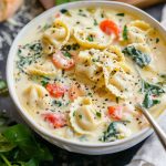 A warm bowl of creamy tortellini soup filled with cheese tortellini, fresh spinach, carrots, and a rich broth, garnished with parsley.