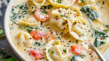 A warm bowl of creamy tortellini soup filled with cheese tortellini, fresh spinach, carrots, and a rich broth, garnished with parsley.