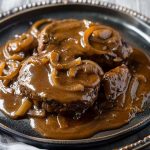 A juicy hamburger steak smothered in rich brown gravy with caramelized onions, served alongside mashed potatoes and green beans.