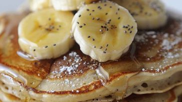 A stack of golden banana pancakes topped with sliced bananas, maple syrup, and a sprinkle of cinnamon, served on a rustic breakfast plate.
