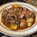 Tender shredded Mississippi pot roast served with gravy, pepperoncini, and mashed potatoes on a rustic plate.