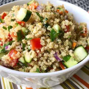A colorful bowl of easy quinoa salad filled with fluffy quinoa, cherry tomatoes, cucumbers, red onion, parsley, and feta cheese, drizzled with lemon vinaigrette.