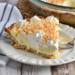 A slice of easy coconut cream pie with a golden crust, fluffy whipped topping, and toasted coconut flakes, served on a white dessert plate.