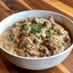 A bowl of creamy beef stroganoff with tender beef strips, mushrooms, and egg noodles, garnished with fresh parsley and served in a rustic dish.