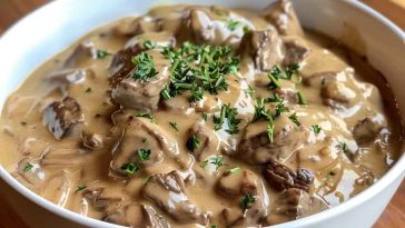 A bowl of creamy beef stroganoff with tender beef strips, mushrooms, and egg noodles, garnished with fresh parsley and served in a rustic dish.