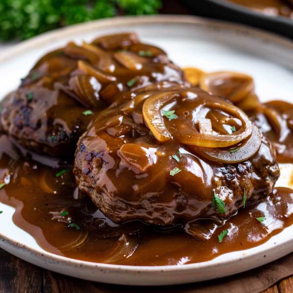 A sizzling hamburger steak smothered in rich brown gravy with caramelized onions, served alongside mashed potatoes and green beans on a rustic dinner plate.