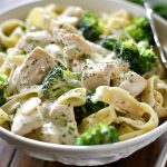 A bowl of creamy Alfredo pasta with tender chicken strips and bright green broccoli florets, topped with Parmesan and fresh herbs.