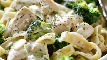 A bowl of creamy Alfredo pasta with tender chicken strips and bright green broccoli florets, topped with Parmesan and fresh herbs.