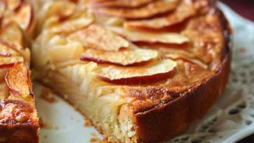 Rustic French apple cake dusted with powdered sugar, served with apple slices and whipped cream on a vintage plate.