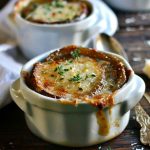 A bowl of French onion soup topped with golden, melted Gruyère cheese and toasted baguette slices, served hot and bubbling.