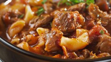 A steaming bowl of classic goulash with elbow macaroni, ground beef, tomatoes, and herbs, garnished with fresh parsley.