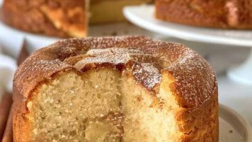 A golden, fluffy cinnamon cake with a buttery crumb and cinnamon-sugar swirl, sliced and served on a rustic plate with a cup of coffee.
