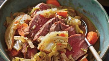A rustic plate of slow-cooked corned beef slices served with tender cabbage, carrots, and potatoes, garnished with parsley.